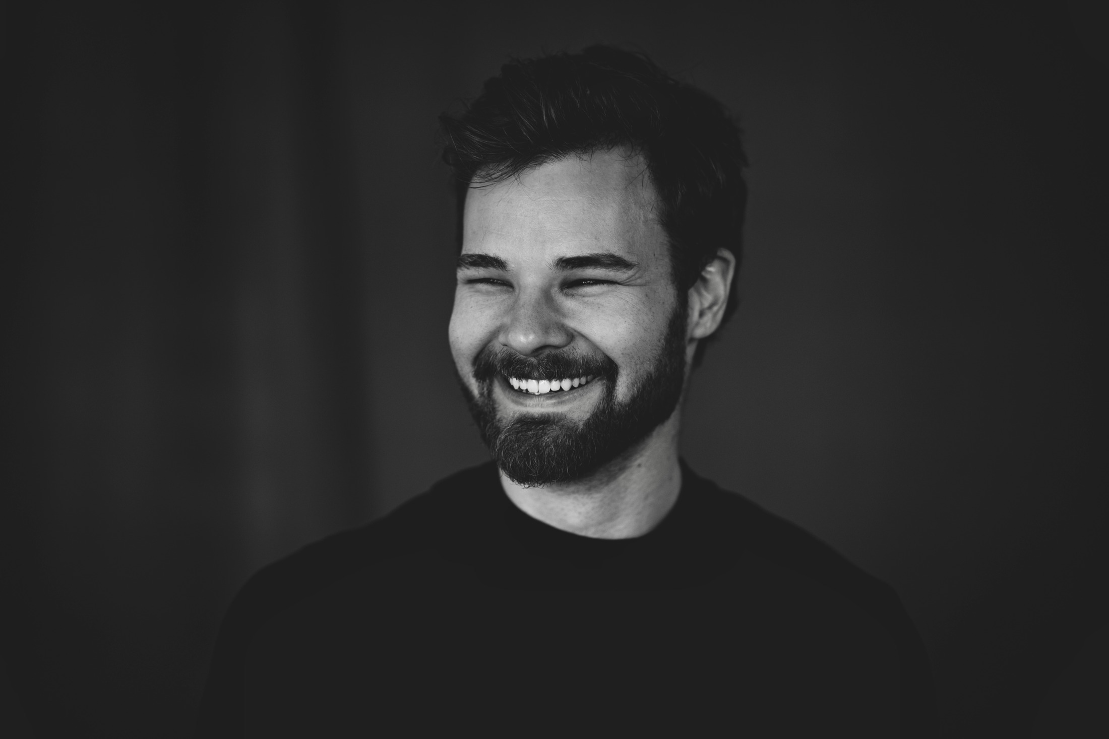 A bearded man laughing in a black-and-white studio portrait