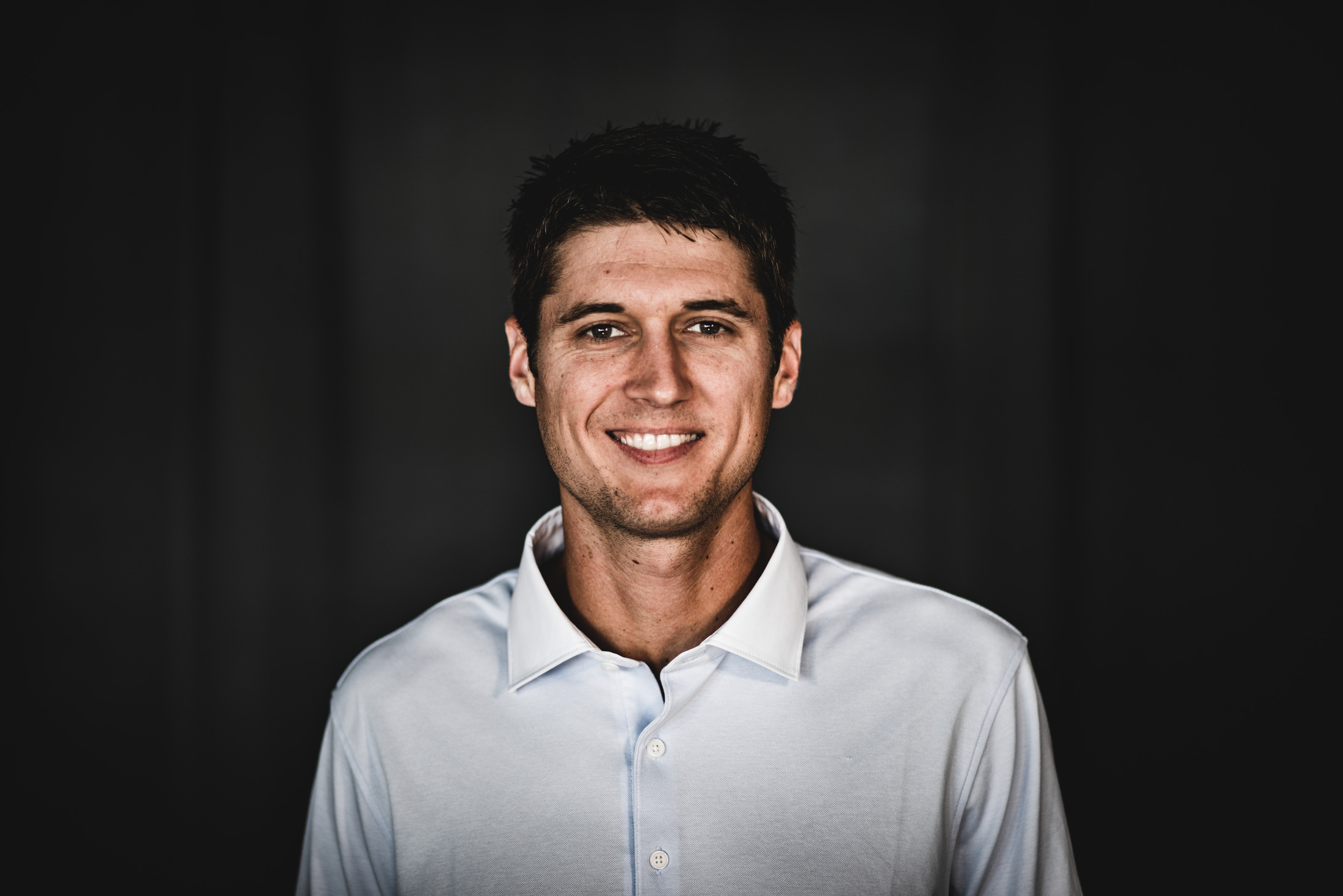 A smiling man in a white shirt against a dark studio background